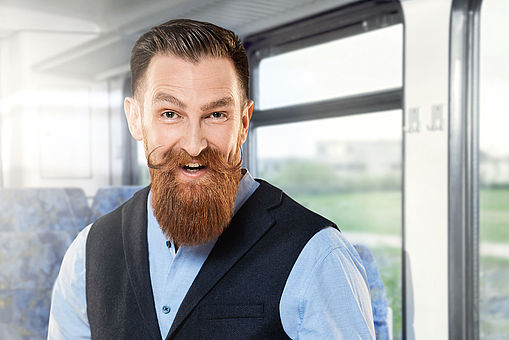 Ein Mann mit Bart steht lachend und mit Handy in der Hand in einem Bus.